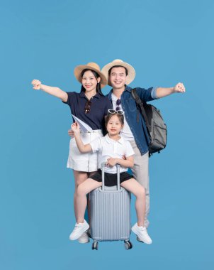 Üç kişilik neşeli bir aile yolculuğa hazır. Kız, mavi bir arka planda bavulun üzerinde oturuyor.