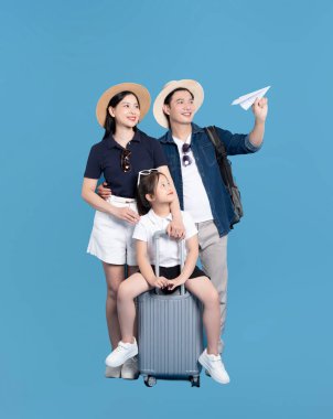 Mutlu aile tatile hazır kız bavulda oturuyor baba elinde kağıt uçak mavi arka plan