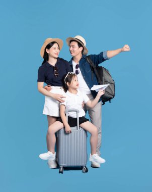 Yolculuğa hazır üç kişilik bir aile, bavul ve kağıt uçakla mavi bir arkaplanda poz veriyor.