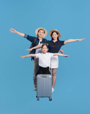 Üç kişilik aile, kolları ve bavulları açık bir uçağı taklit eden mavi bir arkaplanda poz veriyor.