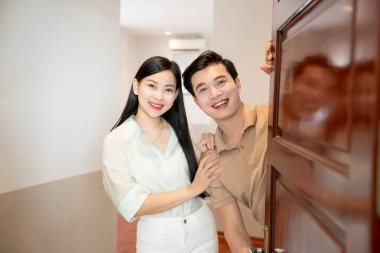 Gülümseyen bir çift, iyi aydınlatılmış bir evde, açık bir kapıdan dışarı bakar ve hoş bir ortam yaratır.