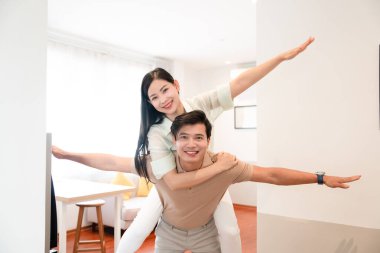 Gülümseyen bir çift, erkeğin sırtında ve kollarını açmış bir kadınla evde eğleniyor.