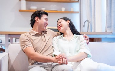 Genç bir çift, modern parlak evlerinde el ele tutuşurken gülümsüyor.