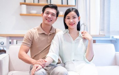 Gülümseyen bir çift evlerindeki bir kanepede rahatlıyor. Konfor ve bağlantı sergiliyorlar.