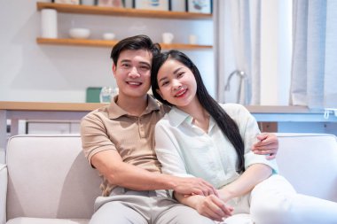 Mutlu bir çift, aydınlık oturma odalarındaki bir kanepede dinleniyor ve sevgi ve neşe gösteriyorlar.