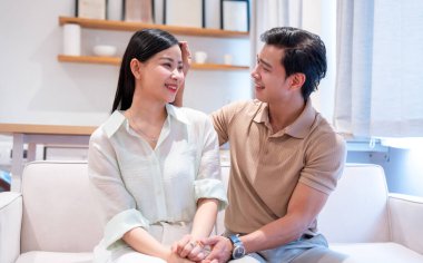 Bir çift kanepede oturuyor adam nazikçe kadının saçına dokunuyor ve ona gülümsüyor.