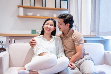 Gülümseyen çift, doğal ışıklandırılmış modern bir oturma odasında hafif bir kanepede sarılır. Yukarıya bakarlar.