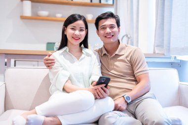 Evde telefonla gülümseyen bir çift rahat kıyafetler yakıyor.