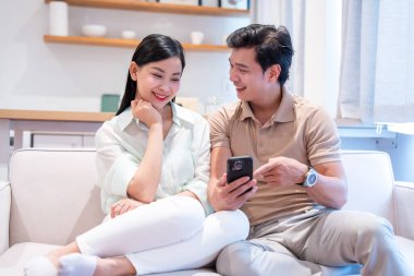 Mutlu bir çift koltukta rahatça oturuyor ve gülümseyen bir cep telefonu ekranına bakıyor.