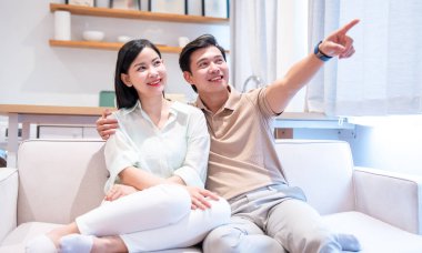 Mutlu bir çift kanepede birlikte otururken gülümser ve adam uzaklığı gösterir.