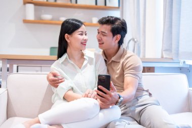 Mutlu bir çift evdeki koltukta otururken cep telefonuna bakar.