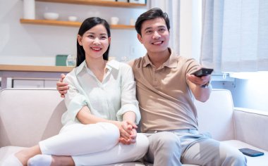 Genç ve mutlu bir çift oturma odalarında televizyon izlerken birlikte kanepede dinleniyorlar.