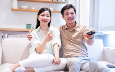 Mutlu çift, rahat modern oturma odalarında kanepede televizyon seyrediyor.