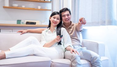 Modern oturma odalarındaki bir kanepede oturup televizyon seyreden ve birlikte vakit geçiren bir çift.