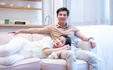 Gülümseyen bir çift açık gri kanepelerinde dinlenir. Kadın ortağının üzerine uzanır.