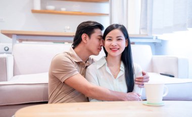 Asyalı çift sıcak bir ortamda kucaklaşır kadın, erkeğin şefkatle eğilmesiyle tatlı tatlı gülümser.