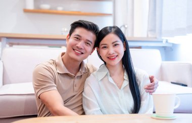 Oturma odasındaki kameraya gülümseyen Asyalı bir çift otururken sahne sıcaktan uçuyor.