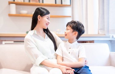 Güzel bir anne ve küçük oğlu, parlak bir oturma odasında, bir kanepede otururken, sevgi dolu bir anı paylaşıyorlar.