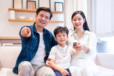 Gülümseyen aile evde rahat vakit geçirmeyi sever. Baba, uzaktan kumandanın annede olduğuna işaret ediyor.