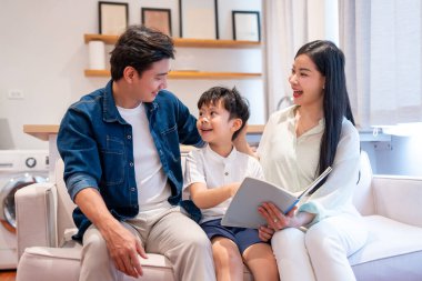 Bir baba ve oğul kanepede birlikte okumaktan zevk alırken birbirlerine gülümserler.