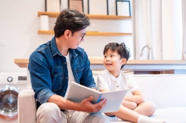 Asyalı bir baba oğluna kitap okuyor. Kapalı alanda bağ kuruyor ve birlikte güzel vakit geçiriyor.
