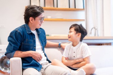 Bir baba ve oğlu bir kanepede oturmuş evde gülüşüyor ve birbirleriyle konuşuyorlar.