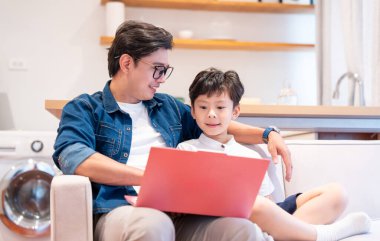 Baba oğul kanepede yan yana oturmuş dizüstü bilgisayarın ekranına bakıyorlar.