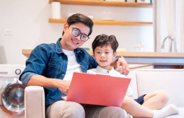 Bir baba ve oğlu dizüstü bilgisayara bakıyorlar. Bir kanepede birlikte oturuyorlar.