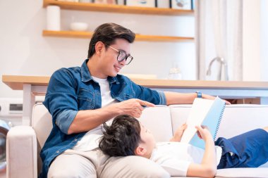 Kanepede çocuğuna kitap okuyan bir ebeveyn evde öğrenme ve iletişim kurma anını paylaşıyor.