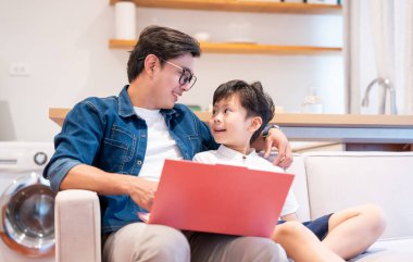 Bir baba ve oğul kanepede dizüstü bilgisayar kullanarak ve birbirlerine bakarak kaliteli zaman geçiriyorlar.