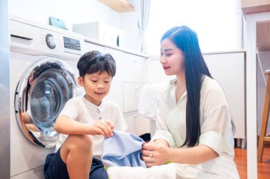 Asyalı anne ve oğlu çamaşırhanede yerde oturup temiz giysileri neşeyle katlıyorlar.
