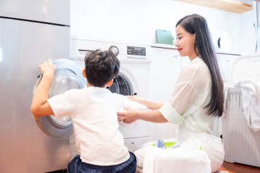 Bir anne ve oğlu birlikte çamaşır yıkıyorlar. Parlak, temiz evlerinde, aletlerin yanında.