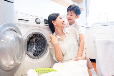 Bir anne ve oğlu, aydınlık ve sevgi dolu bir çamaşır odasında çamaşır yıkıyorlar.