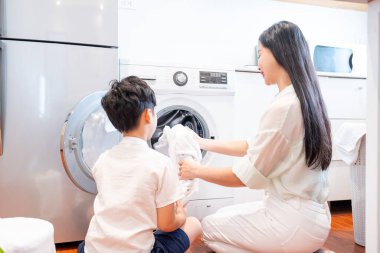 Bir kadın ve bir çocuk çamaşırları çamaşır makinesine yüklüyor.