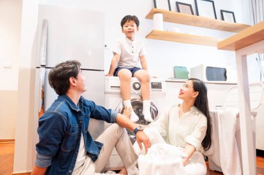 Çamaşır gününde gülümseyen bir aile yerde oturuyor. Çocuk da aletin üstünde oturuyor.