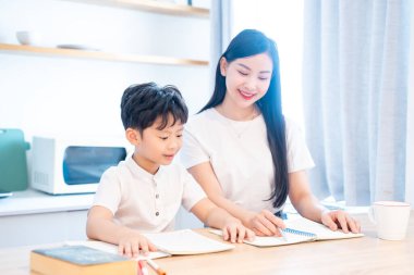 Genç bir çocuk güneşli bir mutfak ortamında yetişkin bir arkadaşının yardımıyla özenle öğreniyor.