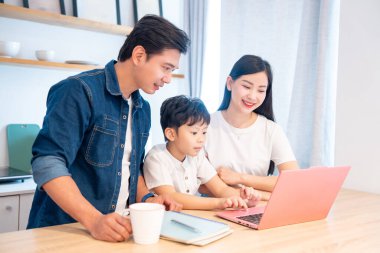 Üç kişilik bir aile bilgisayar kullanarak bir masada oturuyor. Aileler oğullarının öğrenmesini destekliyor.