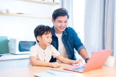 Neşeli bir baba, parlak bir mutfakta oğlunun dizüstü bilgisayarına yardım ediyor. Öğrenme ve aileyi teşvik ediyor.