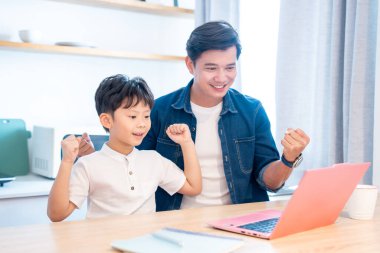 Asyalı bir baba ve oğlu evde heyecanlı bir şekilde çalışıyor ve birlikte gülümsüyorlar.