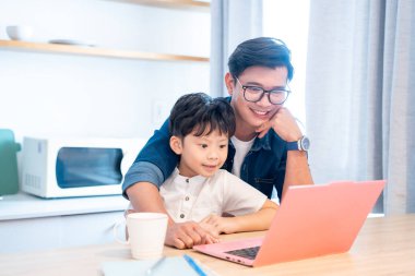 Bir baba ve oğlu, mutfaklarında dizüstü bilgisayarla mutlu mesut vakit geçirirler.