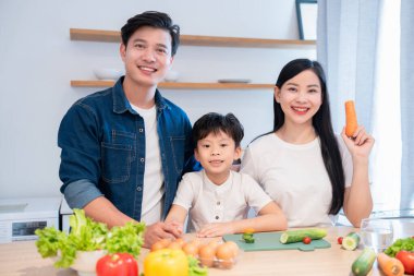 Gülümseyen bir aile taze sebze ve yumurtalarla güzel bir mutfakta sağlıklı bir yemek yapar.