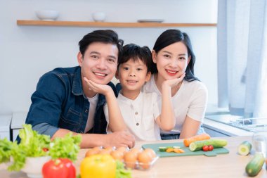 Sevgi dolu bir aile, parlak mutfağında gülümsüyor ve sağlıklı taze sebze yemeği pişirmeye hazırlanıyor.