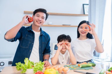 Üç kişilik bir aile mutfakta birlikte yemek hazırlarken eğleniyorlar. Dilimlenmiş sebzeleri tutuyorlar.