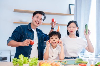 Üç kişilik aile mutfakta ellerinde taze sebzelerle yemeği hazırlarken eğleniyorlar.