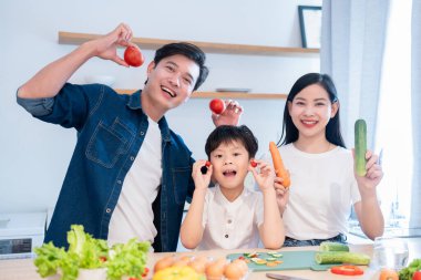 Gülümseyen üç kişilik aile, modern mutfak ortamlarında taze ürünlerle yemek pişirmekten zevk alıyor.