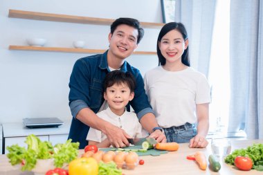Üç kişilik bir aile, açık ve temiz bir mutfak ortamında birlikte sebze hazırlıyor.