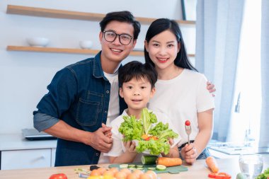 Üç kişilik neşeli bir aile modern mutfaklarında sağlıklı bir yemek için taze yemek hazırlıyorlar.