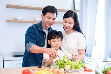 Neşeyle dolu mutfaklarında taze sebze ve sebzelerle salata hazırlayan bir aile.