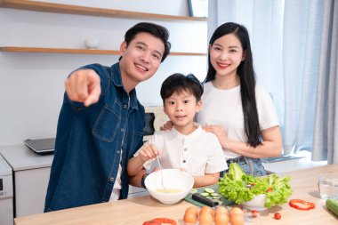 Mutfakta yemek yapan üç kişilik aile tezgahta sebze karıştırır.