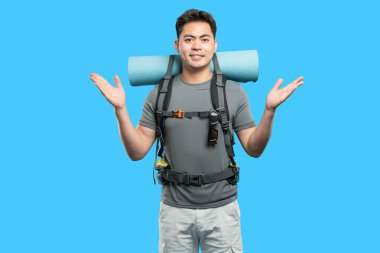 Sırt çantalı ve açık hava kıyafetleri giyen mutlu genç bir adam mavi bir arka planda izole edilir.